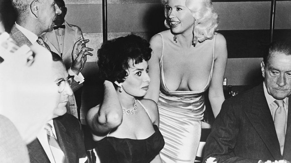 Jayne Mansfield makes an appearance at Sophia Loren's table during a promotional party for Loren, Los Angeles, California, April 12, 1957. 