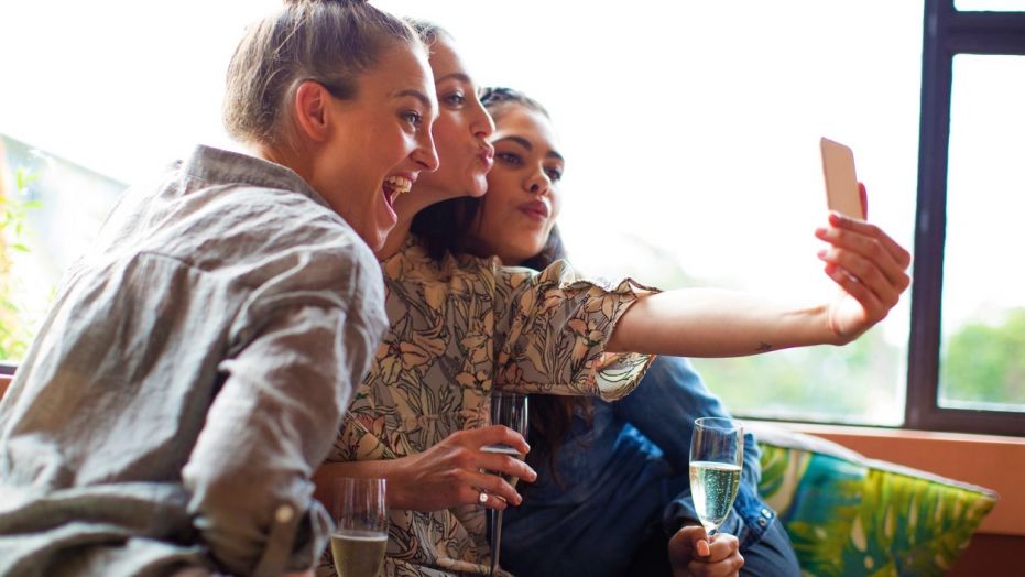 Mixed race girlfriends with Aboriginal woman taking selfie at bar