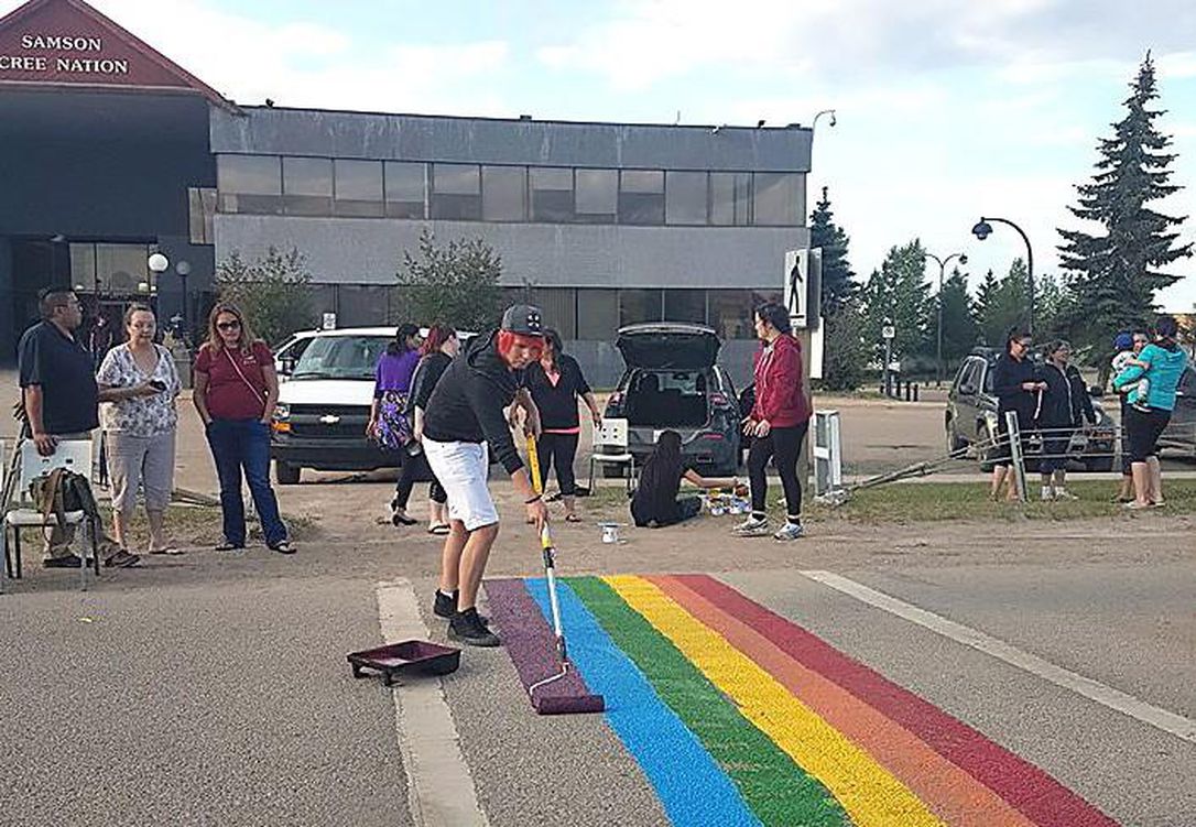 A volunteer helps paint the colourful crosswalk in front of the Samson Cree Nation administration building to celebrate Pride Month in this image provided by the Maskwacis Community. A rainbow crosswalk in an Indigenous community south of Edmonton might be the first one on a First Nation reserve in Canada.